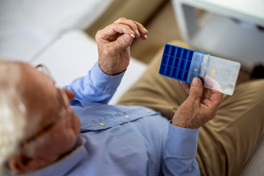 Elderly man arranging his medications in a weekly pill organizer at home.