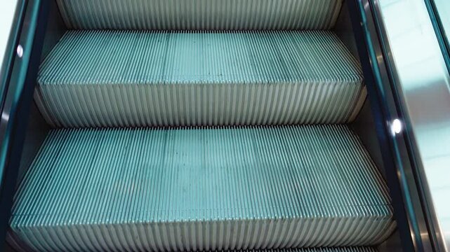 Escalator moving upward inside shopping mall interior. Mechanical steps transporting visitors between floors in modern retail center. Automated vertical transport system operating in commercial space