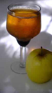 Glass of brut apple cider from Normandy. White table with casting shadows and sunlight. Ripe yellow fruits on the table. Atmospheric mood.