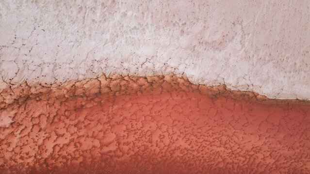 Aerial view of a striking contrast between a stark white salt flat and a vibrant pink lake, creating an otherworldly textured landscape, Yallabatharra, Western Australia, Australia.