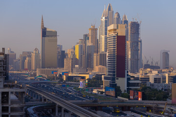 Fototapeta premium Evening view of the city. Orange sunlight, skyscrapers, buildings, and city streets. On the streets of the Emirates, in a public space.