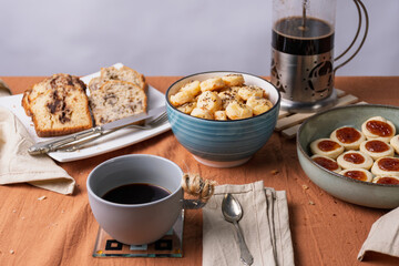 Breakfast or snack with coffee, banana bread, chocolate bread, quince cookies, and cheese cookies with seeds.
