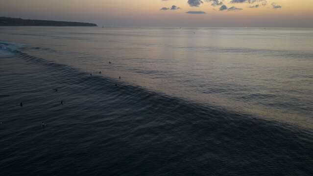 Aerial view of surfers dotting the indigo waters as waves curl under a soft dawn sky, Bali, Bali, Indonesia.