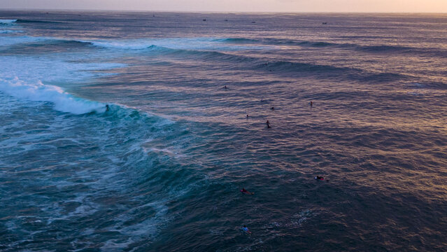 Aerial view of the ocean's turquoise and indigo hues swirl with white foam, dotted by surfers awaiting the perfect wave, Bali, Bali, Indonesia.