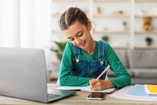 Happy girl student using laptop for distance education, doing homework or enjoying conference video call, watching webinar tutorial, writing notes, studying with teacher, having virtual lesson