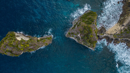 Aerial view of dramatic cliffs meet the turquoise ocean, waves crashing against the rugged coastline, creating a stunning contrast of textures and tones, Nusa Penida, Bali, Indonesia.