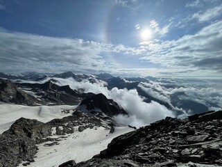 Fototapeta premium Mountain view with clouds and sun shining over snow-capped peaks during daytime in a high altitude setting