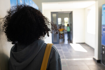 Diverse teenagers standing in school hall, female teen wearing gray hoodie holding yellow strap bag