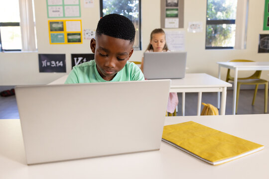 Diverse students working on laptops in class with silver laptop, notebook, green shirt, pink dress