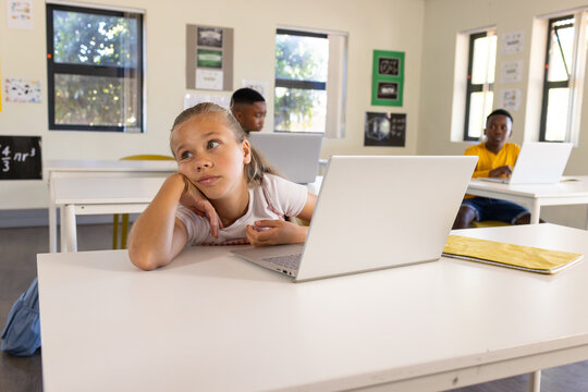 Diverse classmates studying on laptops in classroom with silver laptop and yellow notebook