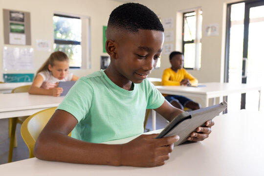 Diverse students sitting in classroom, teenage male African American holding dark tablet, smiling