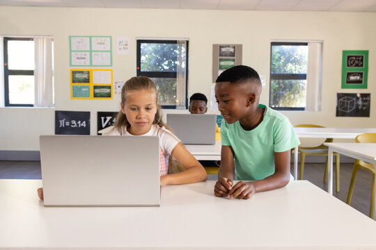 Diverse teenage classmates collaborating in classroom, female youth focusing on laptop screen