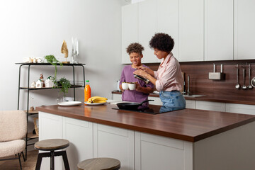 Obraz premium African-American woman and her son prepare chocolate butter and banana sandwiches in the kitchen, while teenager helps his mother prepare breakfast at home.