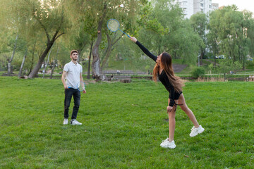 young couple in love playing badminton in the park, guy and girl with rackets playing sports game and actively relaxing outdoors
