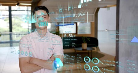 Standing man wearing light-pink shirt, backward cap, arms crossed in office with cyan data on glass