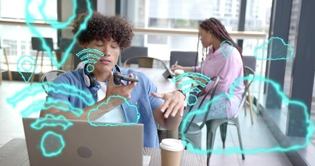 Speaking curly man wearing blue shirt using smartphone at cafe table, laptop and Wi-Fi overlays