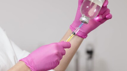 Medical professional in pink gloves prepares a syringe with liquid from a vial, demonstrating the process of drawing medication for cosmetic treatment in a clinical setting