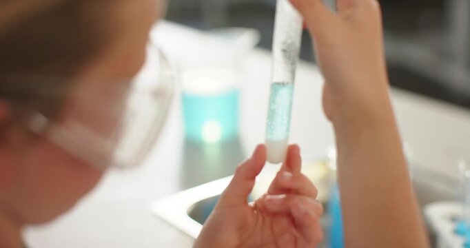 Youth female in goggles seeing sediment raising test tube at bench inspecting turquoise liquid