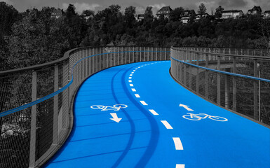 Obraz premium Bicycle lane on a bridge in the city of Tübingen (Germany) with curved, bright blue-colored roadway. Two cycle lanes with white lines and pictograms isolated on dark grayscale background.