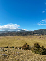 Obraz premium Wide agricultural fields stretch across a Bosnian valley with forested hills in the distance. The image conveys space, sustainability, rural economy, and natural balance.