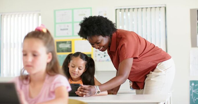 Female teacher and students, teacher seeing child confusion walking leaning guiding tablet at desk