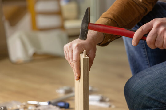 Assembling new furniture. Person assembling furniture with hammer, wooden pieces on floor, copy space