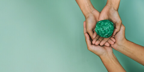 Hands holding green crumpled paper ball on green background symbolize environmental protection, sustainability, recycling, eco friendly business, green energy and climate change awareness concept.