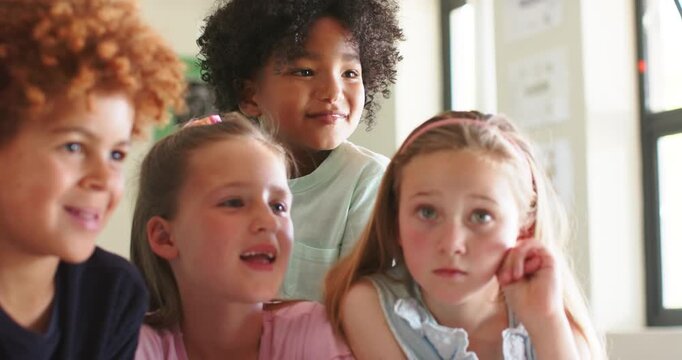 Diverse group of children leaning toward tablet playing funny clip at school, watching and laughing