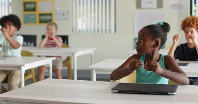 Diverse students following teacher cue, practicing calming breaths in classroom with closed laptop