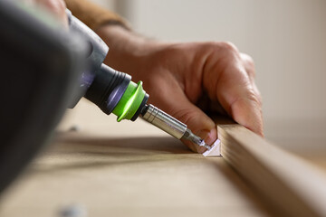 Close-up of a hand using a power drill to fasten a wooden plank on a workbench, showcasing tools...