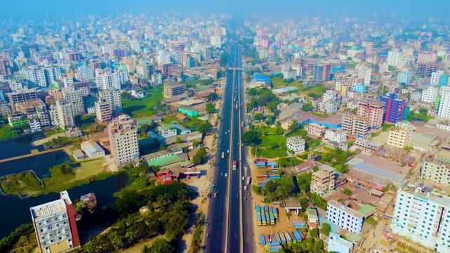 High angle drone footage of a densely populated urban city in Dhaka Matuail, featuring numerous residential buildings, wetlands, and a hazy sky.