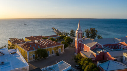 Aerial view of the striking contrast between the red and white church and the yellow buildings against the azure sea, Ilha de Mocambique, Nampula, Mozambique.