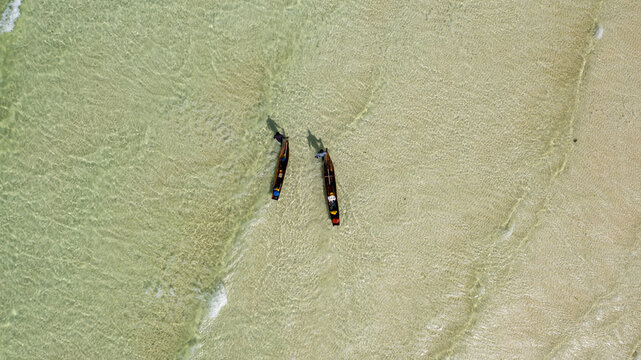 Aerial view of two traditional fishing boats rest on the shore, their dark hulls contrasting with the translucent turquoise waters, Nampula, Nampula Province, Mozambique.