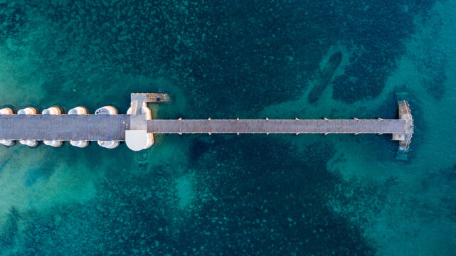 Aerial view of a weathered pier stretching into the turquoise sea, its stone pillars contrasting with the clear water, Ilha de Mocambique, Nampula, Mozambique.