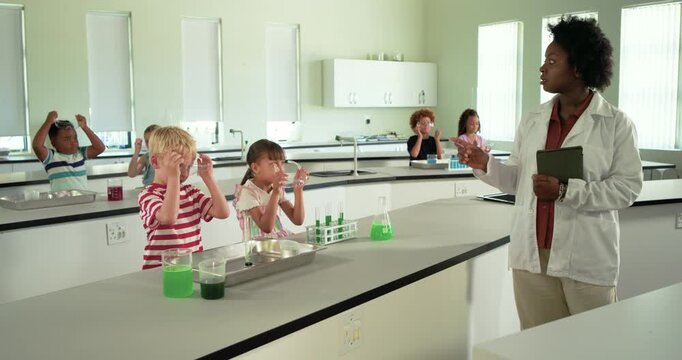 Teacher in lab coat pointing, instructing children at lab don goggles, watch green mix, copy space
