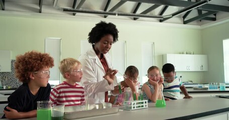 African American woman teacher guiding children with goggles using pipette moving into tubes in lab - Powered by Adobe