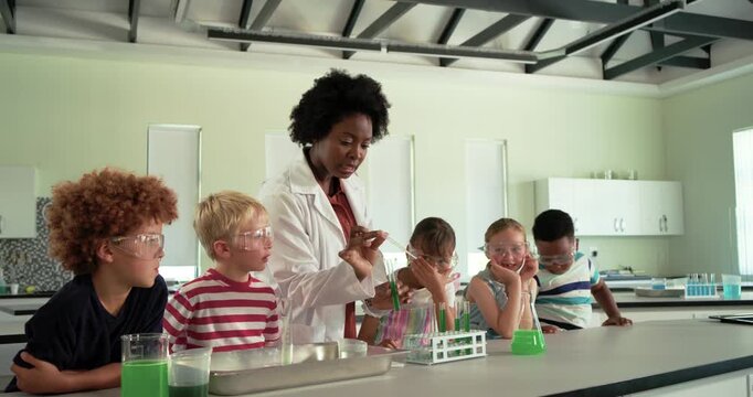 African American woman teacher guiding children with goggles using pipette moving into tubes in lab