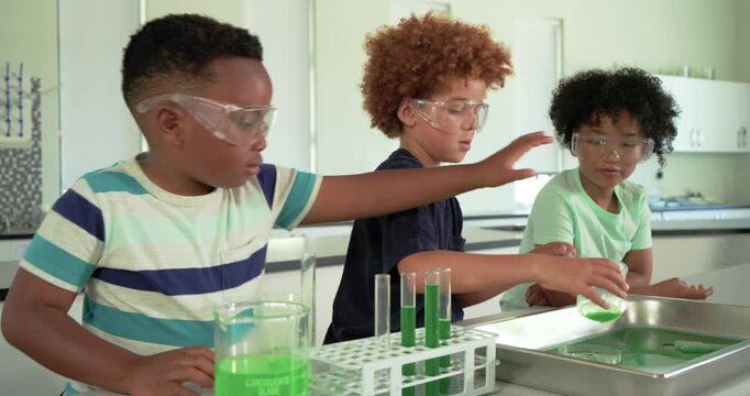 African American male children prompted by lab, pouring green liquid into test tubes to fill rack