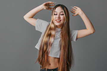 Young woman with long straight hair smiling with eyes closed and raised hands in casual crop top...