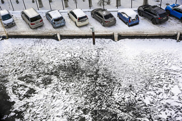 Top view of snow covered cars in street parking lot during winter. This urban winter scene features a row of parked passenger vehicles, with deep tire and foot tracks. © Dina Luk