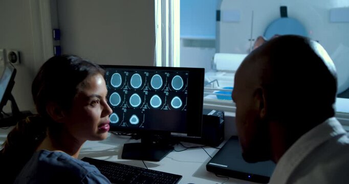 MRI scanner sending images, African American tech and doctor reviewing scans for care at monitor