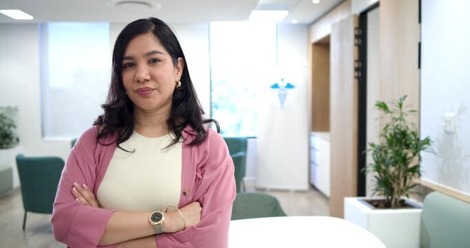 Woman posing in office after pause, folding arms, looking, smiling while at camera in pink cardigan