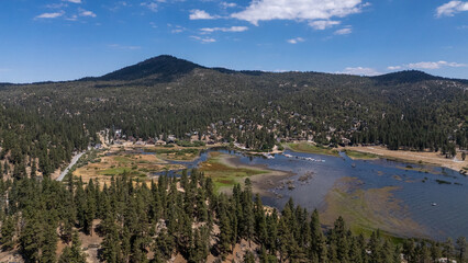 Aerial view of a serene lake reflecting the azure sky, surrounded by dense evergreen forests and a majestic mountain backdrop, Big Bear Lake, California, United States.