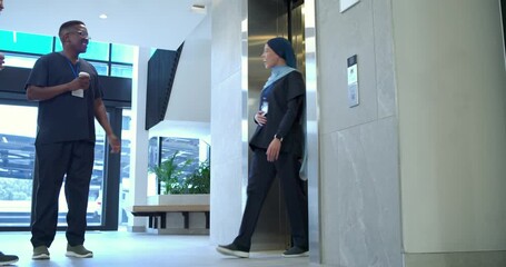 Diverse scrub team entering lobby greeting coworker by elevator with cup and IDs heading to work