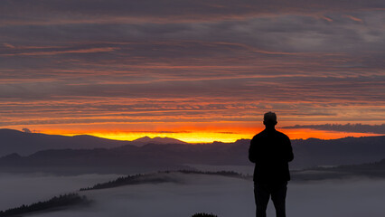 Aerial view of a solitary figure silhouetted against a breathtaking sunset over rolling hills shrouded in ethereal mist, Salmon Creek, California, United States.