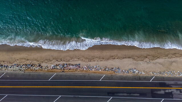 Aerial view of the Pacific Coast Highway running parallel to the sandy beach where the turquoise sea gently meets the shore, Malibu, California, United States.