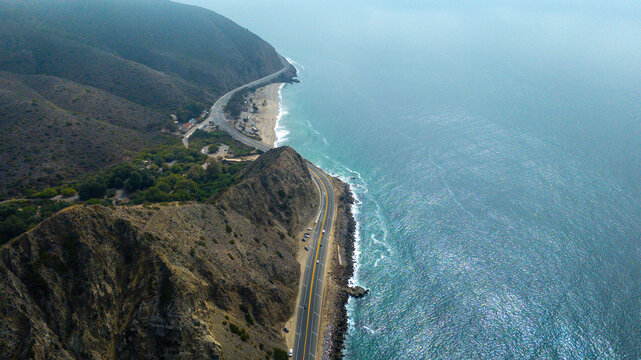 Aerial view of the Pacific Coast Highway snaking along the rugged coastline where the cliffs meet the vast blue ocean, Malibu, California, United States.