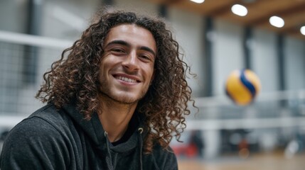 Obraz premium Young caucasian male smiling in gym with volleyball in background.