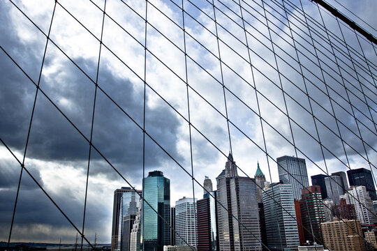 Aerial view of skyscrapers piercing through a dramatic sky, framed by intricate steel cables, a symphony of urban strength and atmospheric beauty, Manhattan, New York, United States.