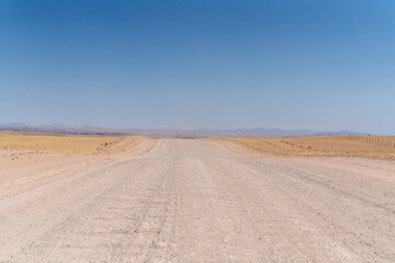 On the way to Swakopmund, an endless road stretches through the striking landscape of the Namib Desert. Vast open plains, arid terrain, and gentle sand dunes meet a wide, dramatic sky.